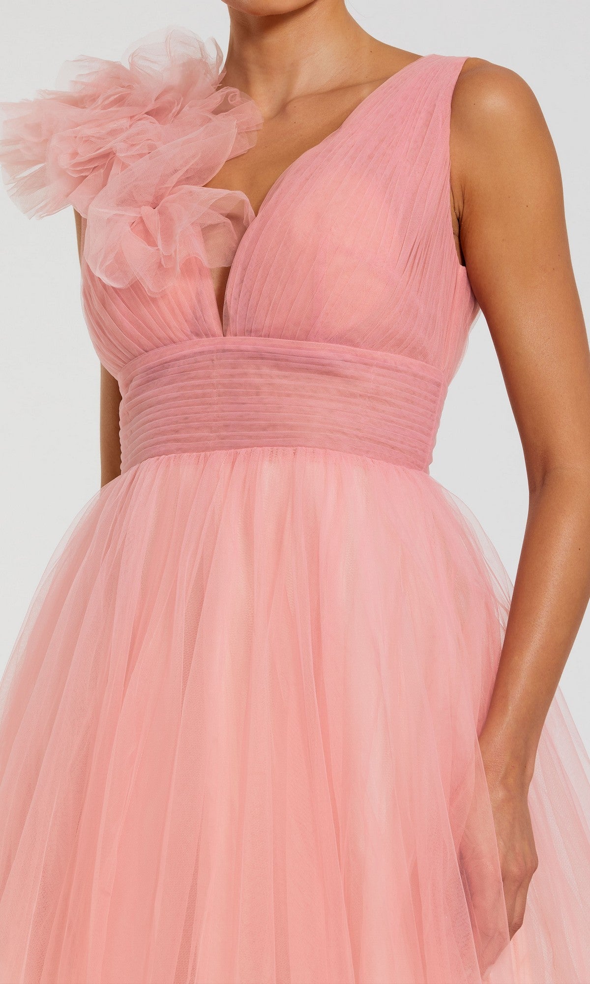A woman wears the Mac Duggal 37001 Long Formal Dress, a sleeveless light pink tulle ballgown with a deep V-neck and a floral ruffle detail on one shoulder.